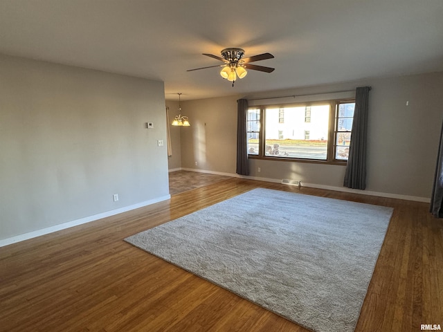 empty room with ceiling fan with notable chandelier and dark hardwood / wood-style flooring