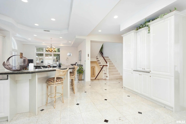 kitchen featuring white cabinets, a breakfast bar area, dark stone counters, and a chandelier