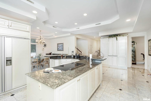 kitchen featuring black electric stovetop, a large island, a raised ceiling, and dark stone counters