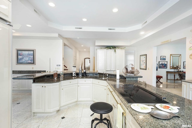 kitchen with sink, white cabinets, a raised ceiling, and dark stone countertops