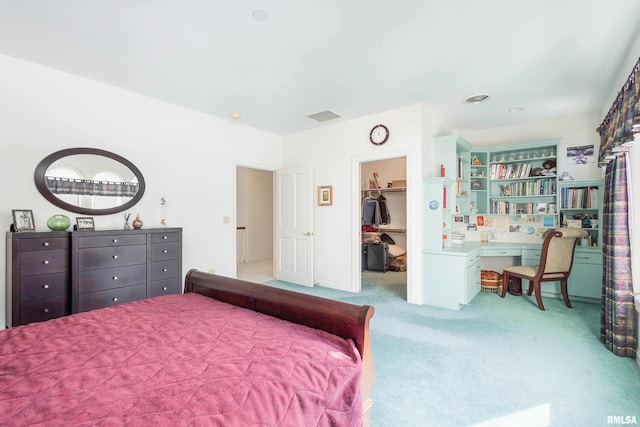 bedroom with light carpet, a walk in closet, a closet, and built in desk