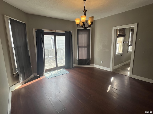 empty room with a textured ceiling, baseboards, wood finished floors, and an inviting chandelier