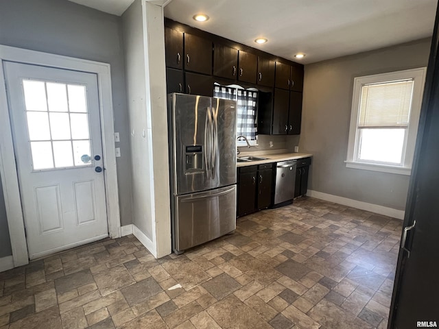 kitchen with baseboards, stone finish floor, appliances with stainless steel finishes, light countertops, and a sink