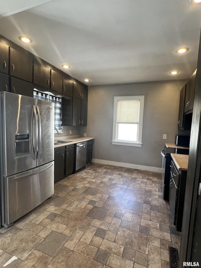 kitchen with a sink, stainless steel appliances, light countertops, and baseboards