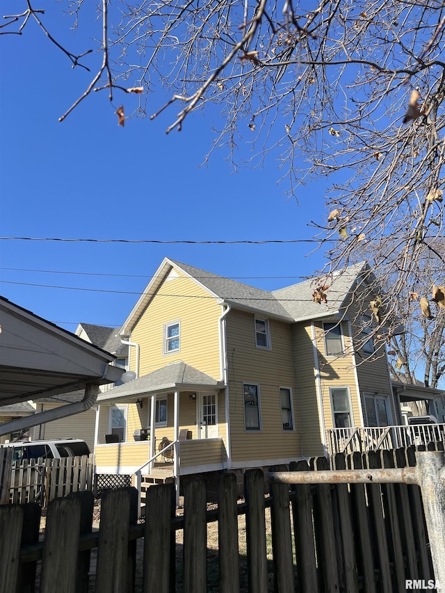 view of side of home featuring a fenced front yard and roof with shingles