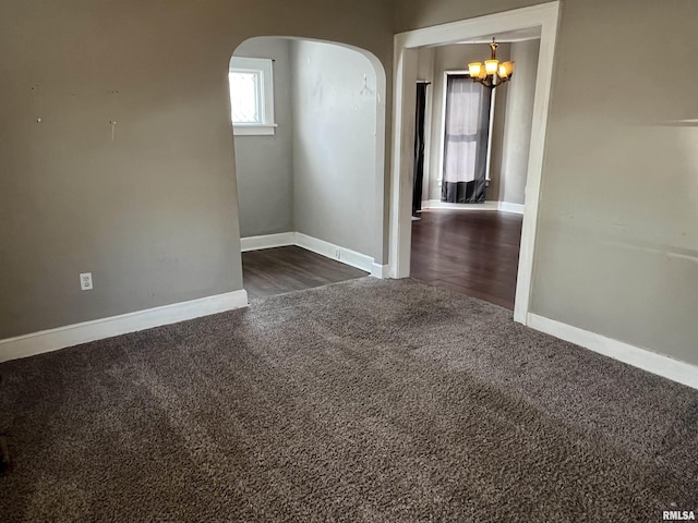 unfurnished room featuring arched walkways, dark carpet, and baseboards