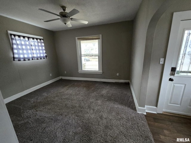 carpeted empty room with arched walkways, a textured ceiling, a ceiling fan, and baseboards