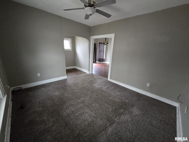 interior space with a ceiling fan, dark colored carpet, arched walkways, and baseboards