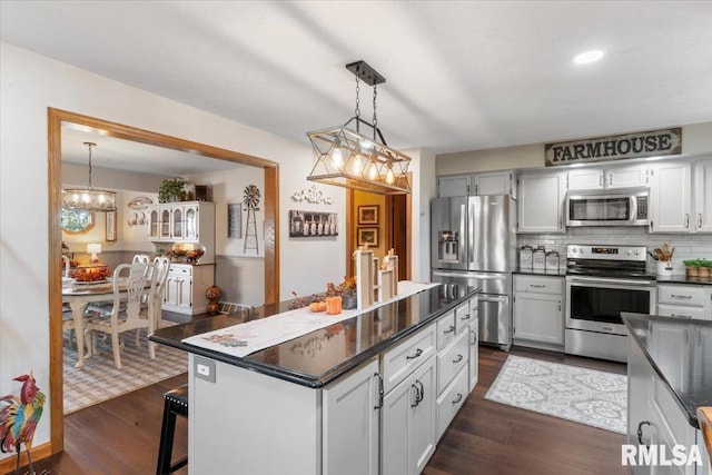 kitchen with stainless steel appliances, a center island, dark hardwood / wood-style floors, hanging light fixtures, and a breakfast bar area