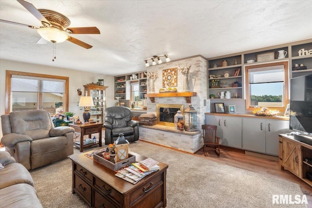 living room with ceiling fan, a fireplace, light hardwood / wood-style floors, and a textured ceiling