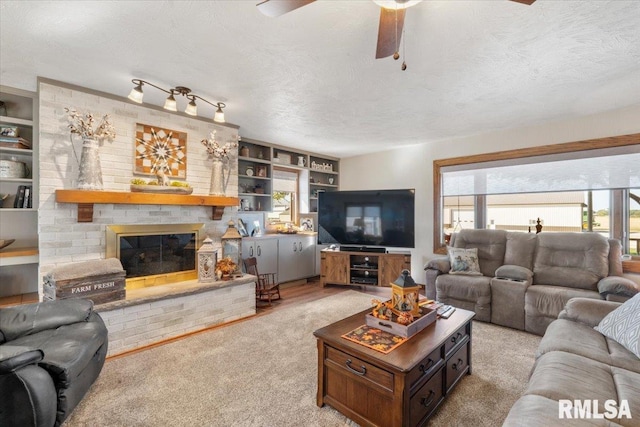 living room featuring ceiling fan, light colored carpet, a textured ceiling, and a brick fireplace