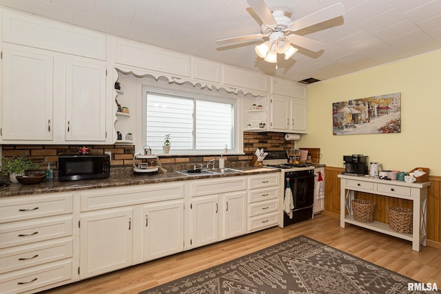 kitchen with white gas range, sink, light hardwood / wood-style flooring, backsplash, and dark stone countertops