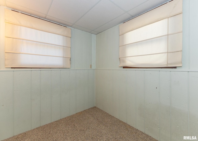 carpeted spare room featuring a paneled ceiling and wood walls