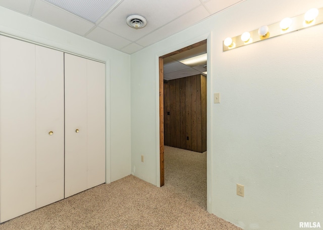 unfurnished bedroom featuring light carpet, a paneled ceiling, and a closet