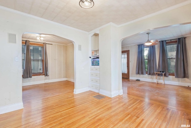 empty room featuring a chandelier, light wood-type flooring, and crown molding