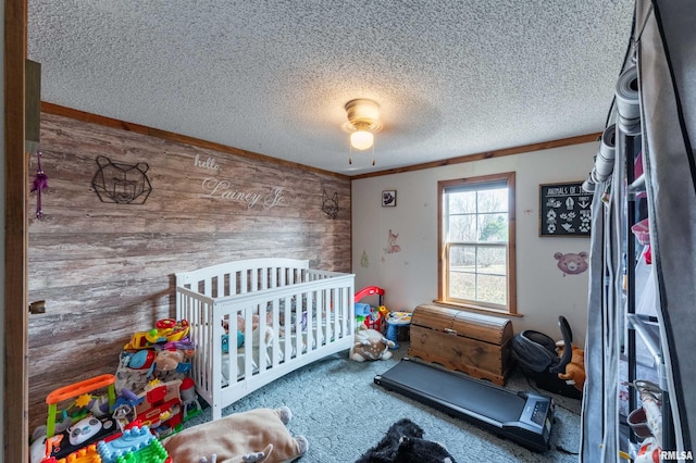 carpeted bedroom with ceiling fan, ornamental molding, wooden walls, and a nursery area