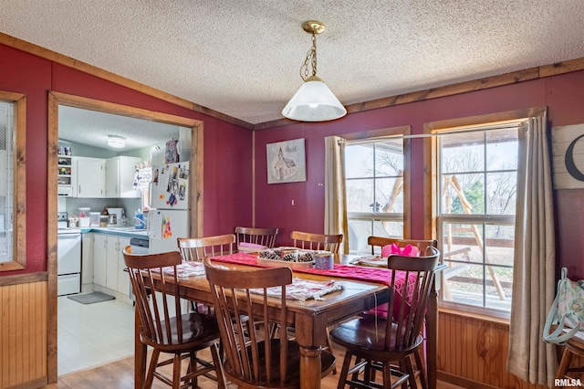 dining room with a textured ceiling, vaulted ceiling, wooden walls, sink, and light hardwood / wood-style floors