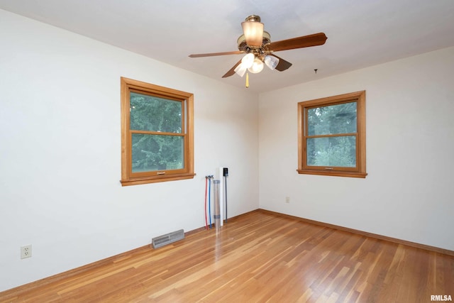 empty room featuring a ceiling fan, visible vents, baseboards, and wood finished floors