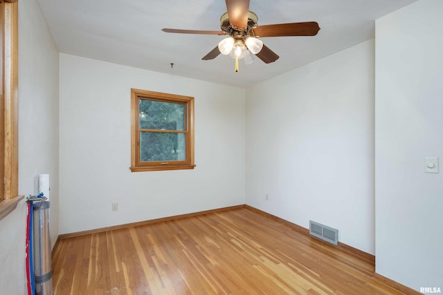 empty room with light wood finished floors, a ceiling fan, visible vents, and baseboards