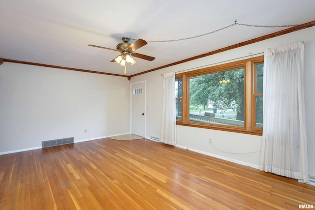 spare room with ceiling fan, wood finished floors, visible vents, baseboards, and crown molding