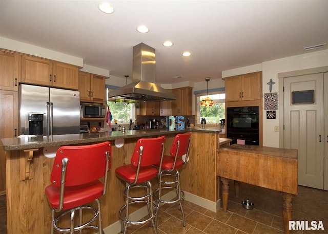 kitchen with pendant lighting, dark tile patterned floors, island range hood, a kitchen bar, and stainless steel appliances