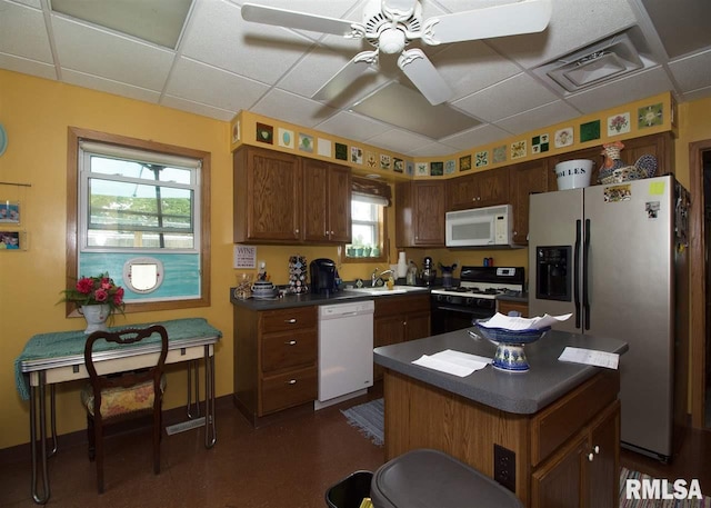 kitchen featuring ceiling fan, a drop ceiling, sink, white appliances, and a kitchen island