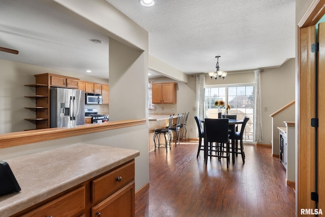 kitchen with appliances with stainless steel finishes, a textured ceiling, an inviting chandelier, dark hardwood / wood-style floors, and hanging light fixtures