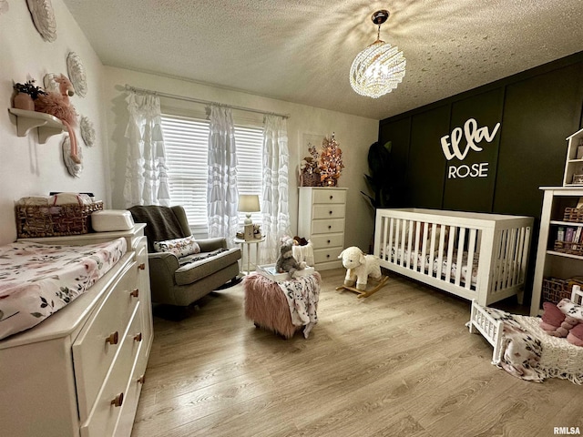 bedroom featuring a notable chandelier, a crib, wood-type flooring, and a textured ceiling