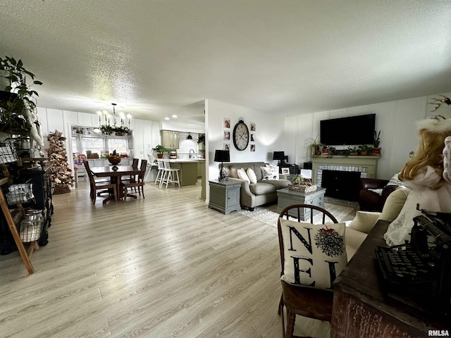 living room with a textured ceiling, a notable chandelier, a fireplace, and light hardwood / wood-style flooring