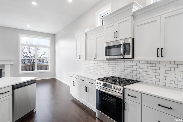 kitchen featuring white cabinets, stainless steel appliances, a fireplace, and dark wood-type flooring