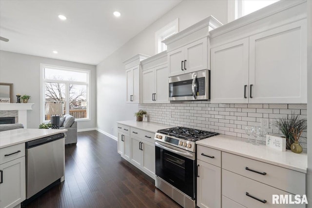 kitchen with dark wood-type flooring, a stone fireplace, decorative backsplash, white cabinetry, and stainless steel appliances