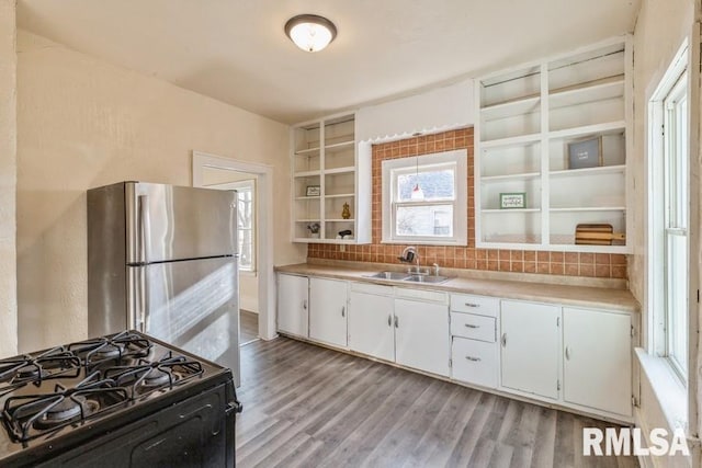 kitchen with stainless steel refrigerator, white cabinetry, sink, black range with gas stovetop, and light wood-type flooring