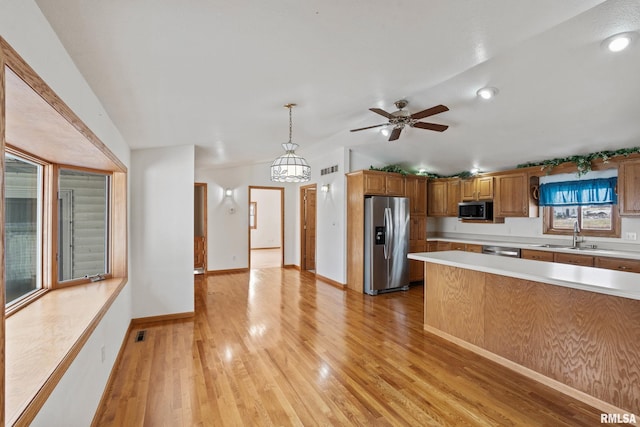 kitchen with pendant lighting, vaulted ceiling, appliances with stainless steel finishes, ceiling fan with notable chandelier, and light wood-type flooring