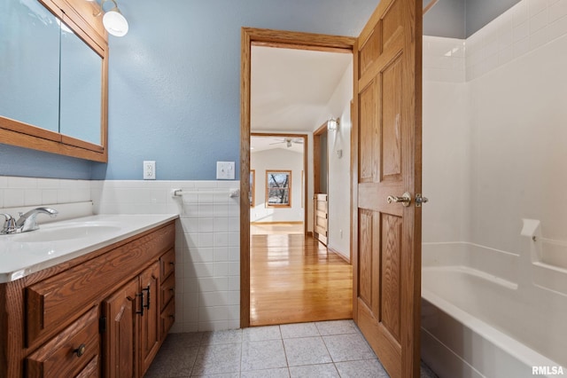 bathroom featuring tile patterned floors, vanity, ceiling fan, tile walls, and washtub / shower combination