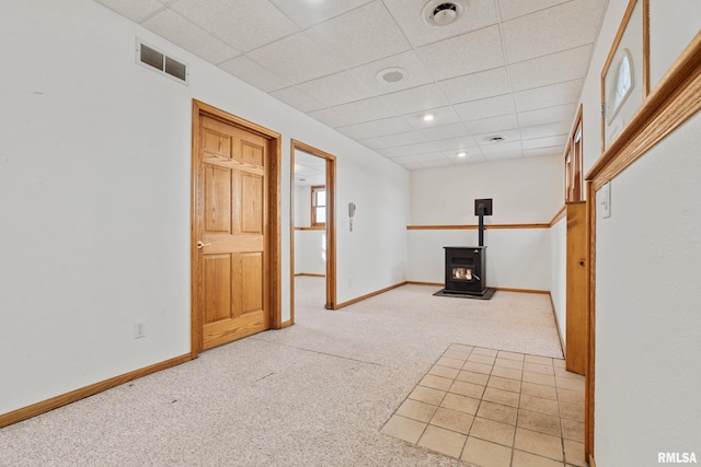 basement featuring a wood stove, light carpet, and a drop ceiling