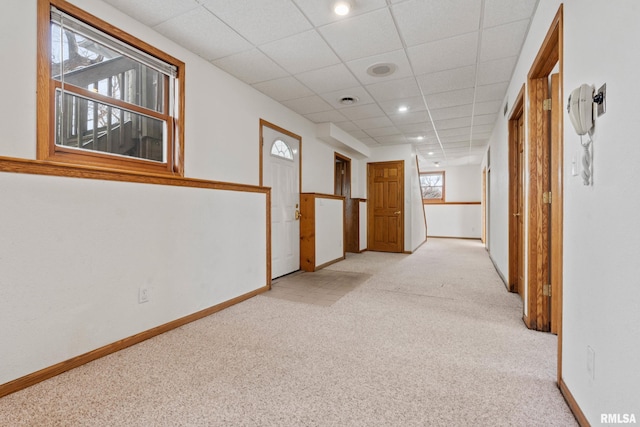 corridor with a paneled ceiling and light colored carpet