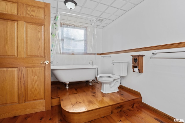 bathroom featuring wood-type flooring, toilet, a drop ceiling, and a tub