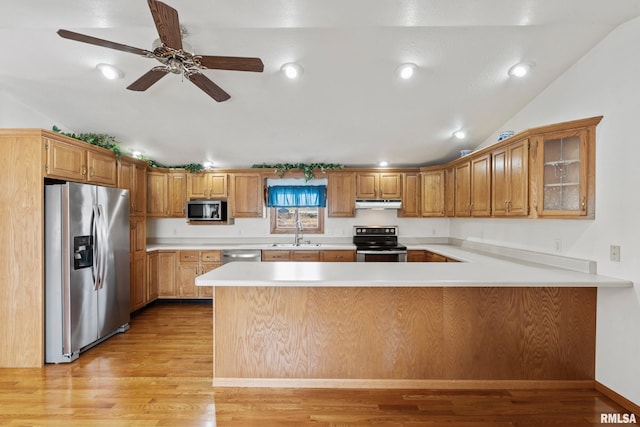 kitchen with kitchen peninsula, appliances with stainless steel finishes, light wood-type flooring, vaulted ceiling, and sink