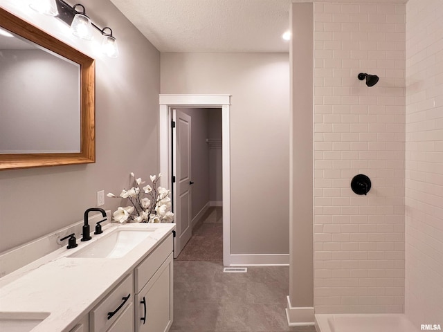 bathroom featuring a textured ceiling, tiled shower, and vanity