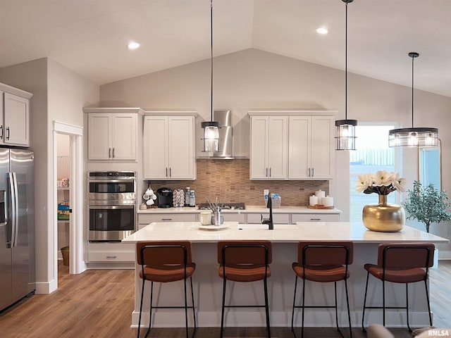 kitchen with stainless steel appliances, an island with sink, wall chimney range hood, and decorative backsplash