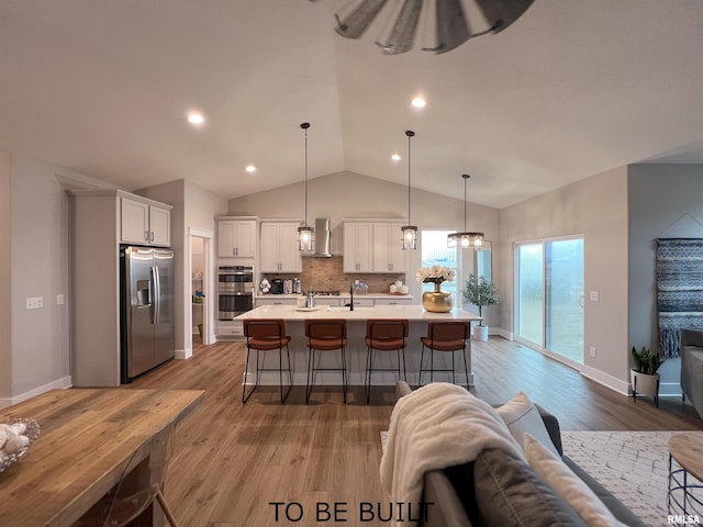 kitchen featuring appliances with stainless steel finishes, an island with sink, white cabinetry, decorative light fixtures, and tasteful backsplash