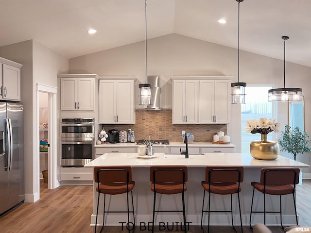 kitchen with stainless steel appliances, wall chimney range hood, backsplash, and an island with sink