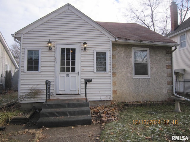 rear view of property with entry steps, a shingled roof, and stucco siding