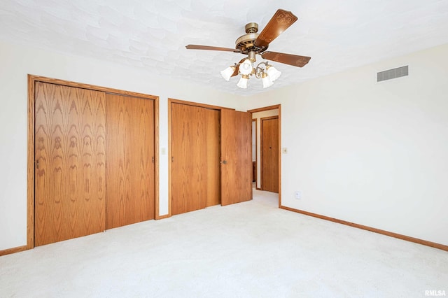 unfurnished bedroom with ceiling fan, light carpet, and two closets