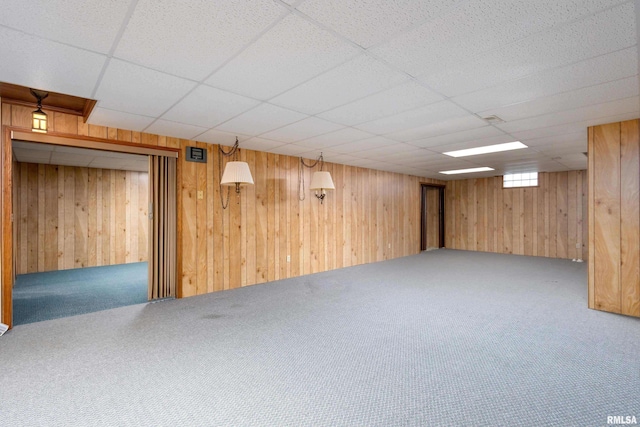 basement featuring carpet flooring, a drop ceiling, and wood walls