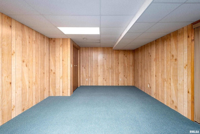 carpeted empty room with a drop ceiling and wooden walls