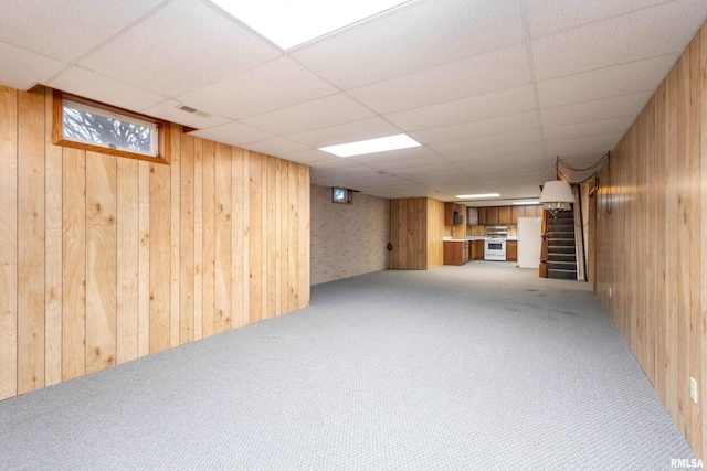 basement featuring a paneled ceiling, light carpet, wood walls, and white refrigerator