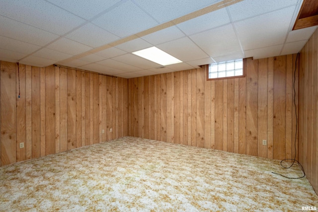 basement with a paneled ceiling, carpet flooring, and wood walls