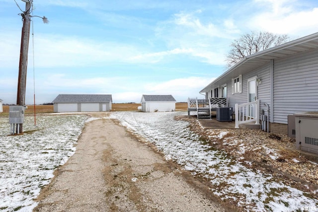 yard covered in snow with a garage, cooling unit, and an outdoor structure