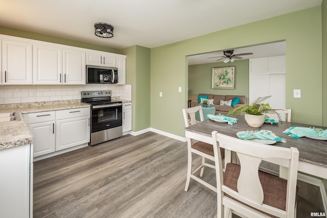 kitchen with appliances with stainless steel finishes, backsplash, light wood-type flooring, ceiling fan, and white cabinets